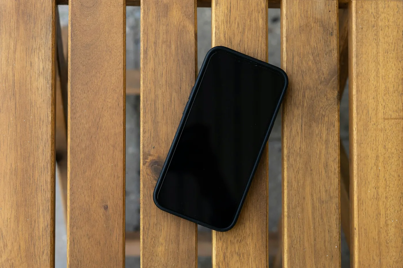 画面が暗いスマートフォンが板張りの机に置かれている