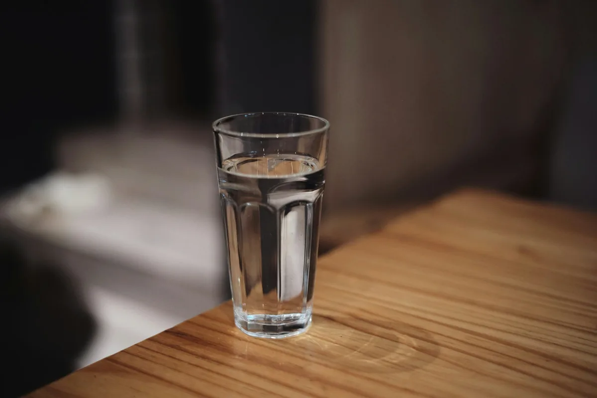 明るい部屋の窓辺で、コップに水を注ぐ手元