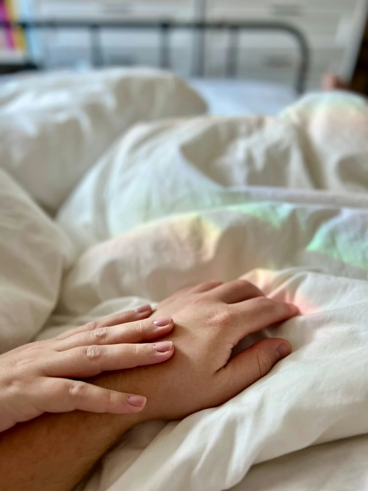 ベッドで横になっている人の手に、家族が手を重ねている