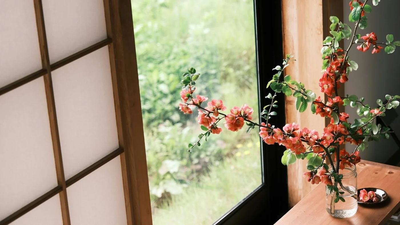 障子のある窓辺。ガラス瓶に活けた花と、その向こうの庭