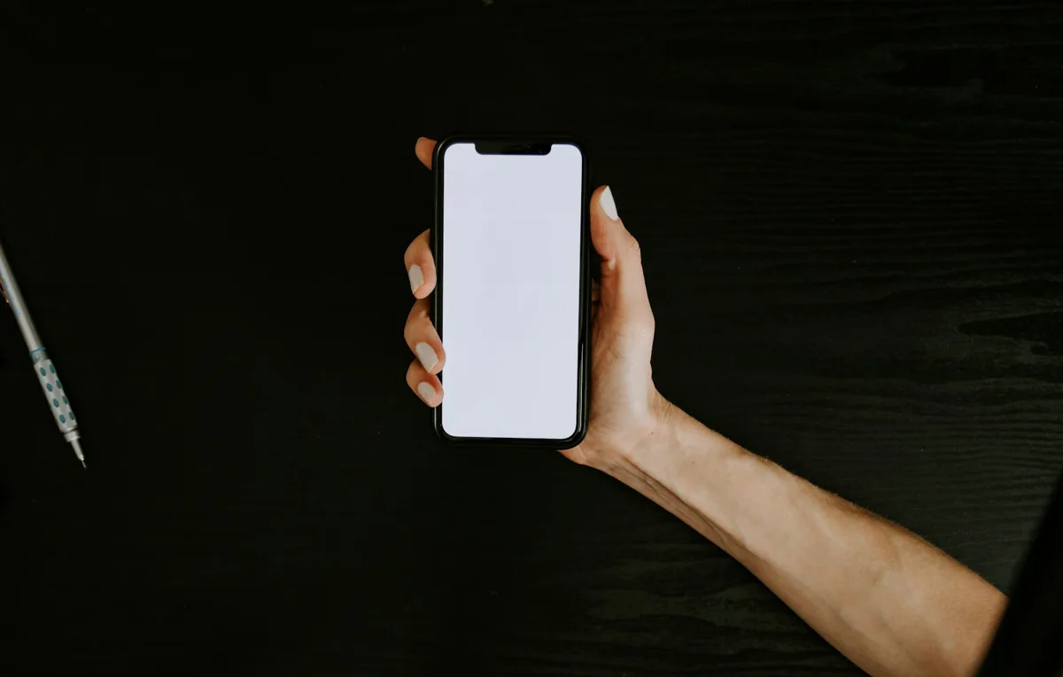暗い机の上で画面のついていないスマートフォンを片手で持っている手元