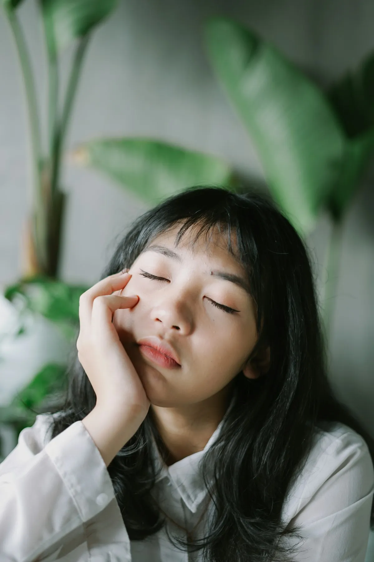 室内で体調がすぐれない様子で顔に手を当てている女性