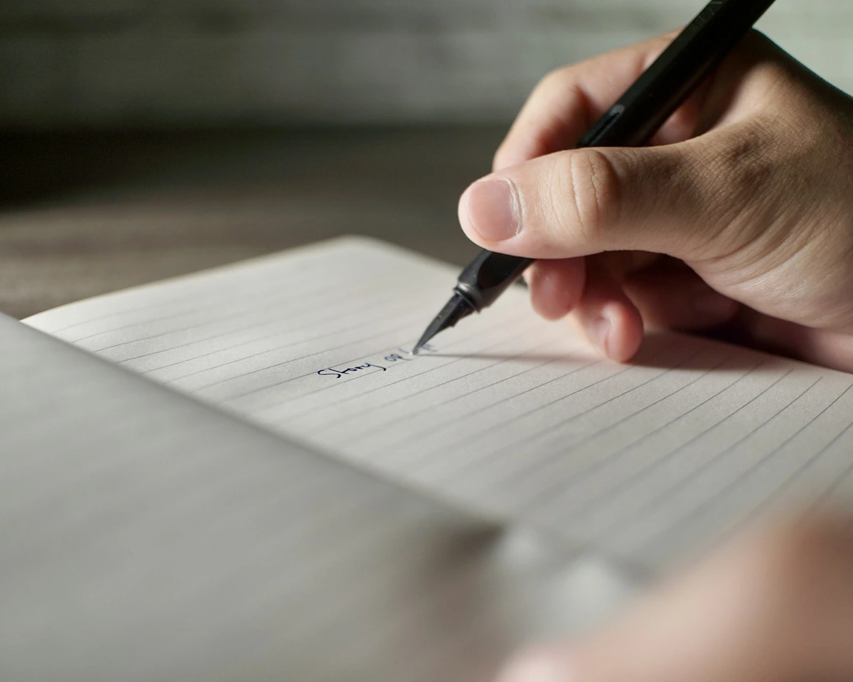 罫線のノートにペンで書き込んでいる手元
