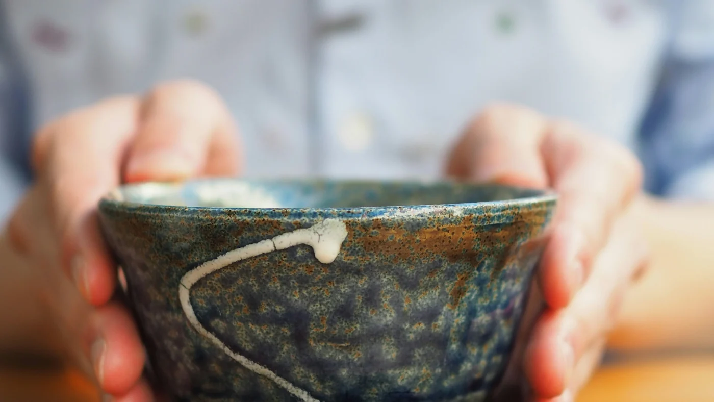 両手で陶器の湯のみを包むように持っている手元。顔は写っていない