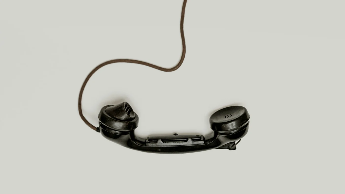 淡い色の面に置かれた黒い電話の受話器。コードが上へ伸びている