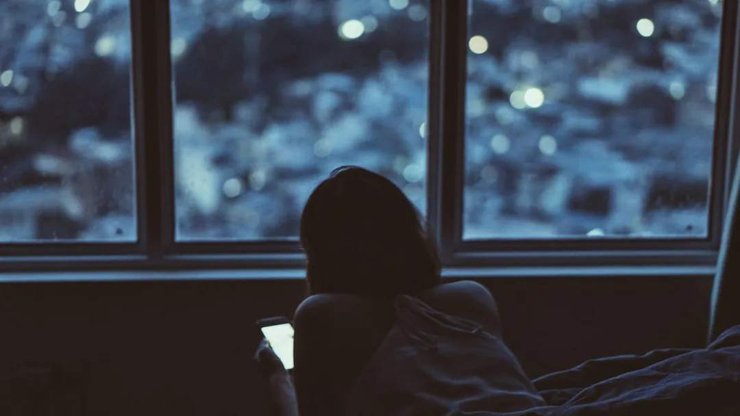夜の窓辺で、スマートフォンの明かりだけがついている