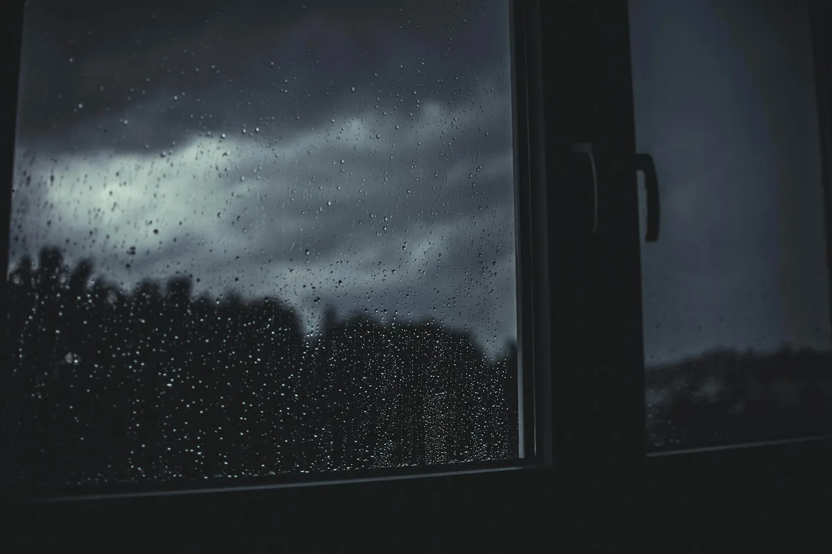 窓の内側から見た、雨と黒い雲におおわれた外の空
