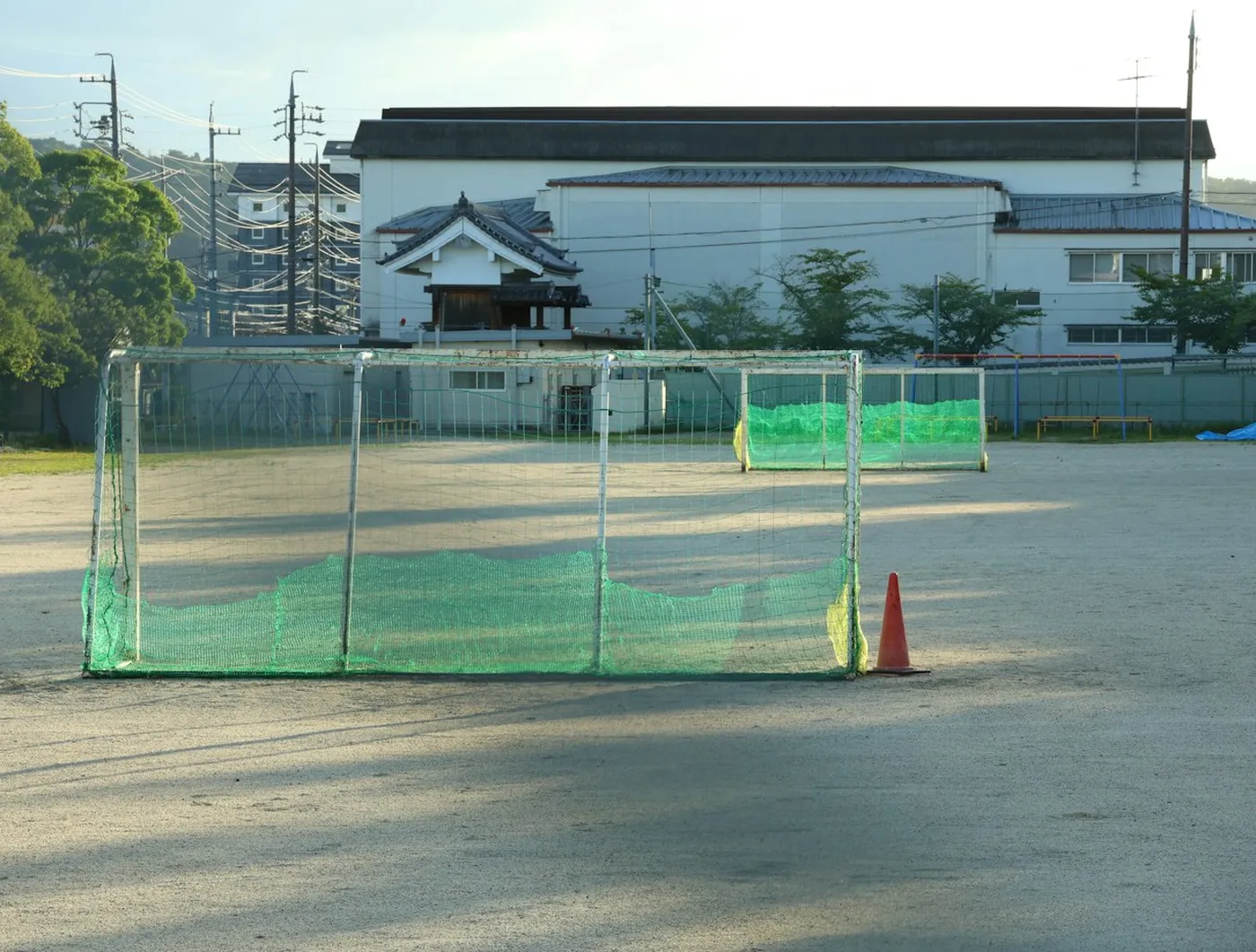 夕方の土の校庭に置かれた、緑のネットのゴールとコーン