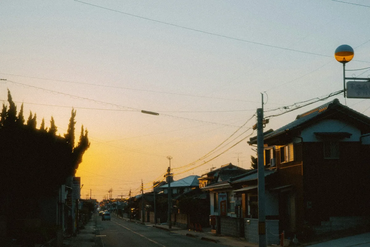 夕暮れの住宅街。瓦屋根の家並みと電柱、オレンジ色の空