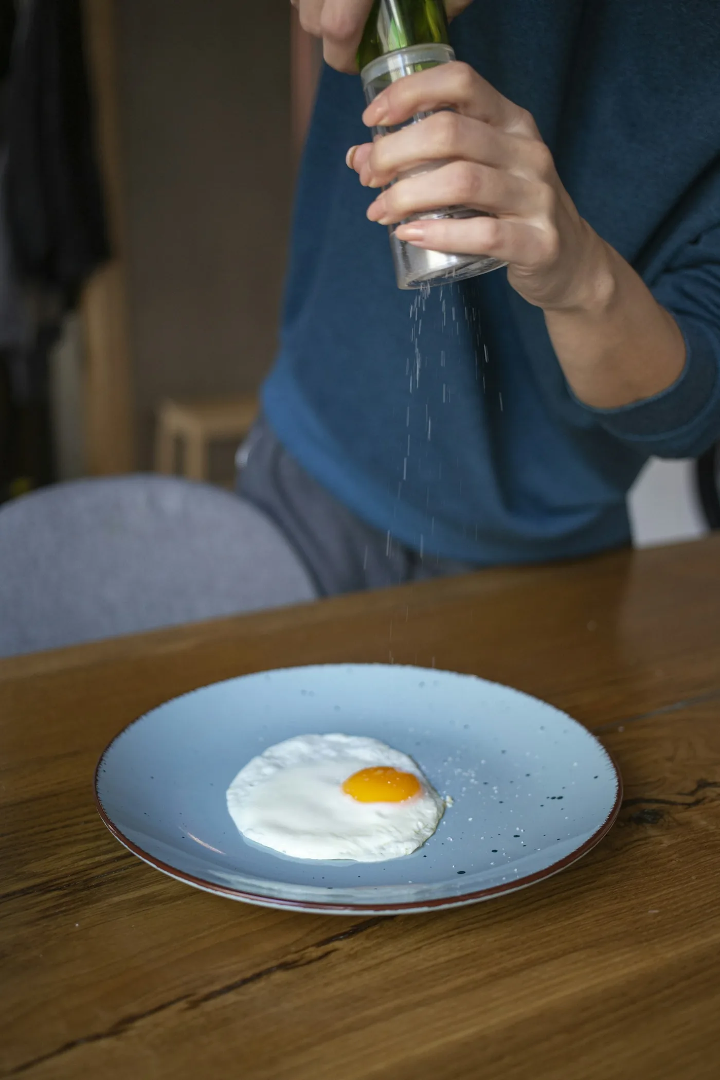 青いシャツの人がテーブルの上の目玉焼きに塩をふっている手元