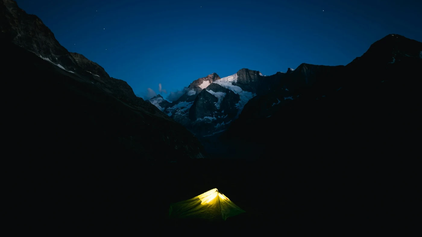 夜の山。暗い稜線の手前に、中から明かりの灯ったテントがひとつ見える