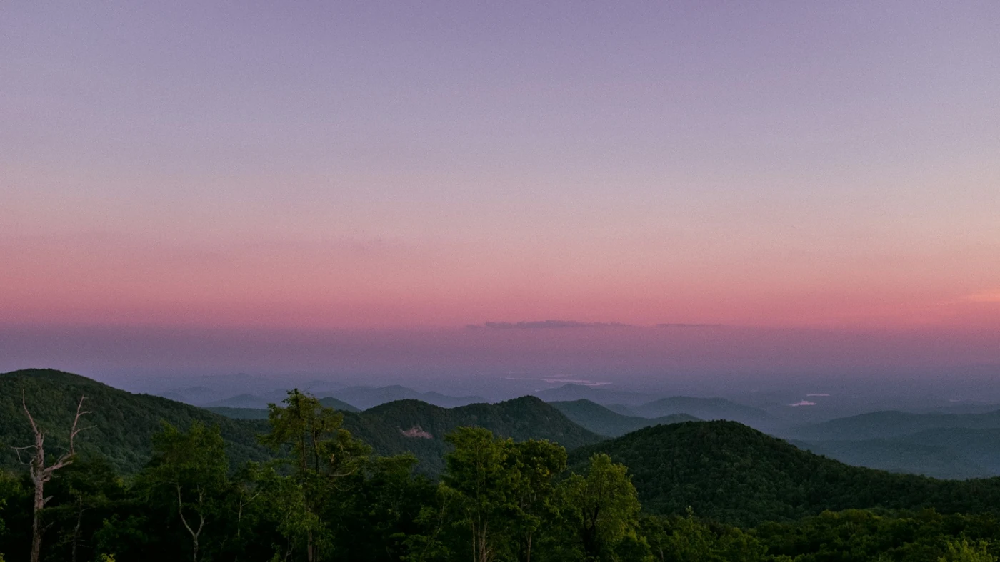 夕暮れの山並みを高いところから見たところ。幾重もの尾根がピンク色の空に溶けている