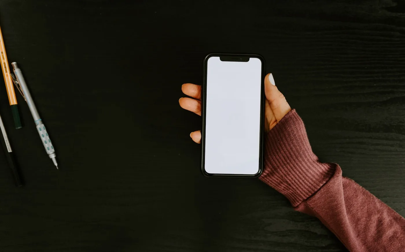 暗い机の上で、片手にスマートフォンを持っている手元