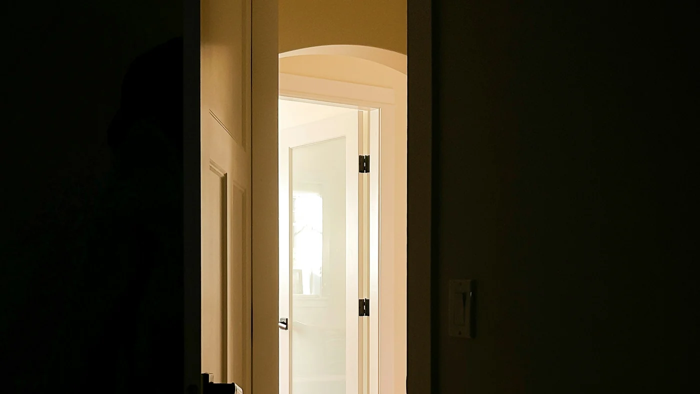 暗い部屋から見た半開きのドア。隣の部屋の明かりが漏れて、床を照らしている